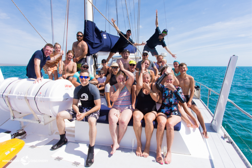 A group of people smiling on a catamaran on the ocean. 